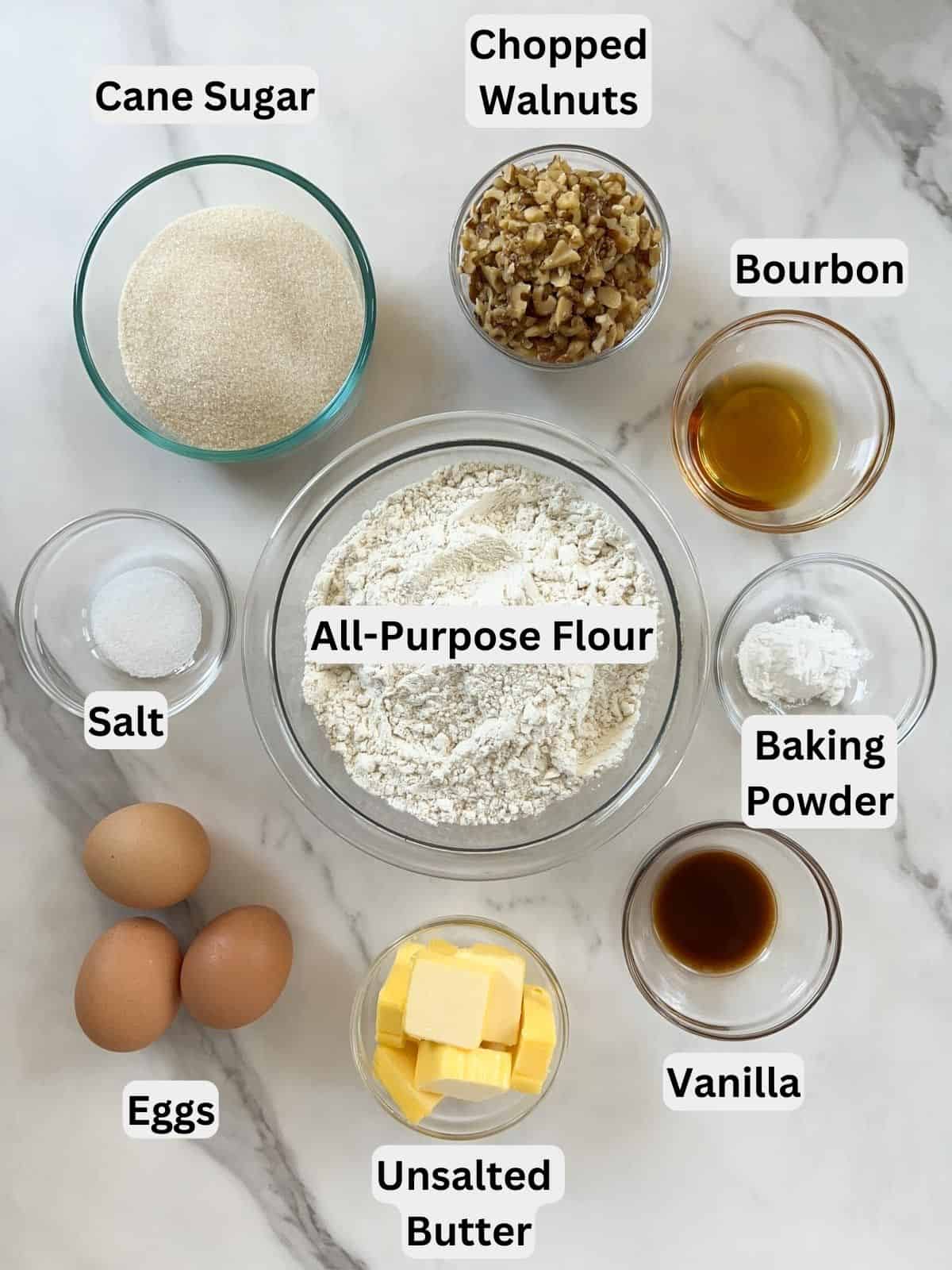 Sugar, walnuts, bourbon, baking powder, vanilla, butter, eggs, salt, and flour measured in glass bowls.