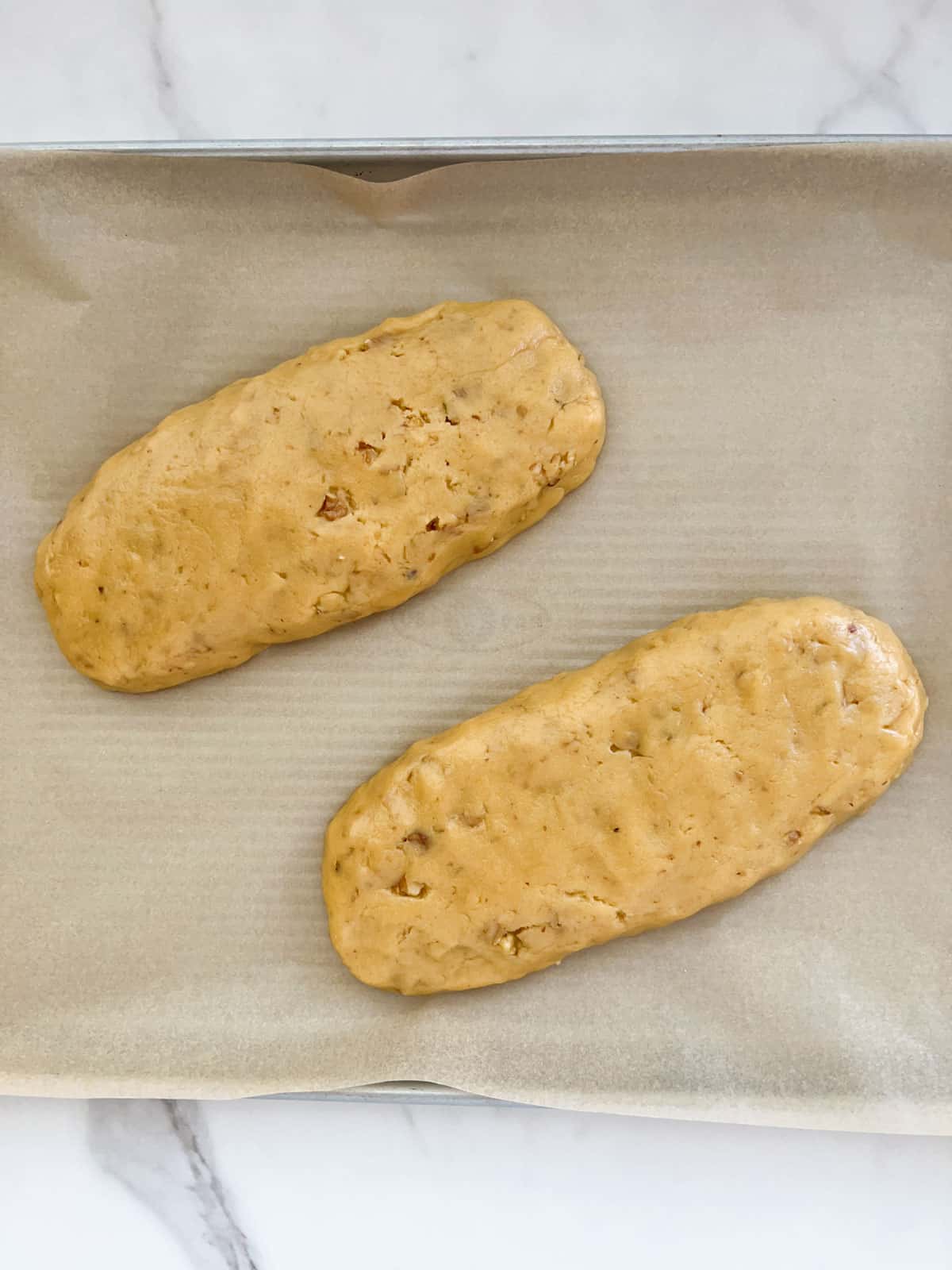 Two logs of biscotti dough placed diagonally on a metal baking sheet lined with parchment paper.