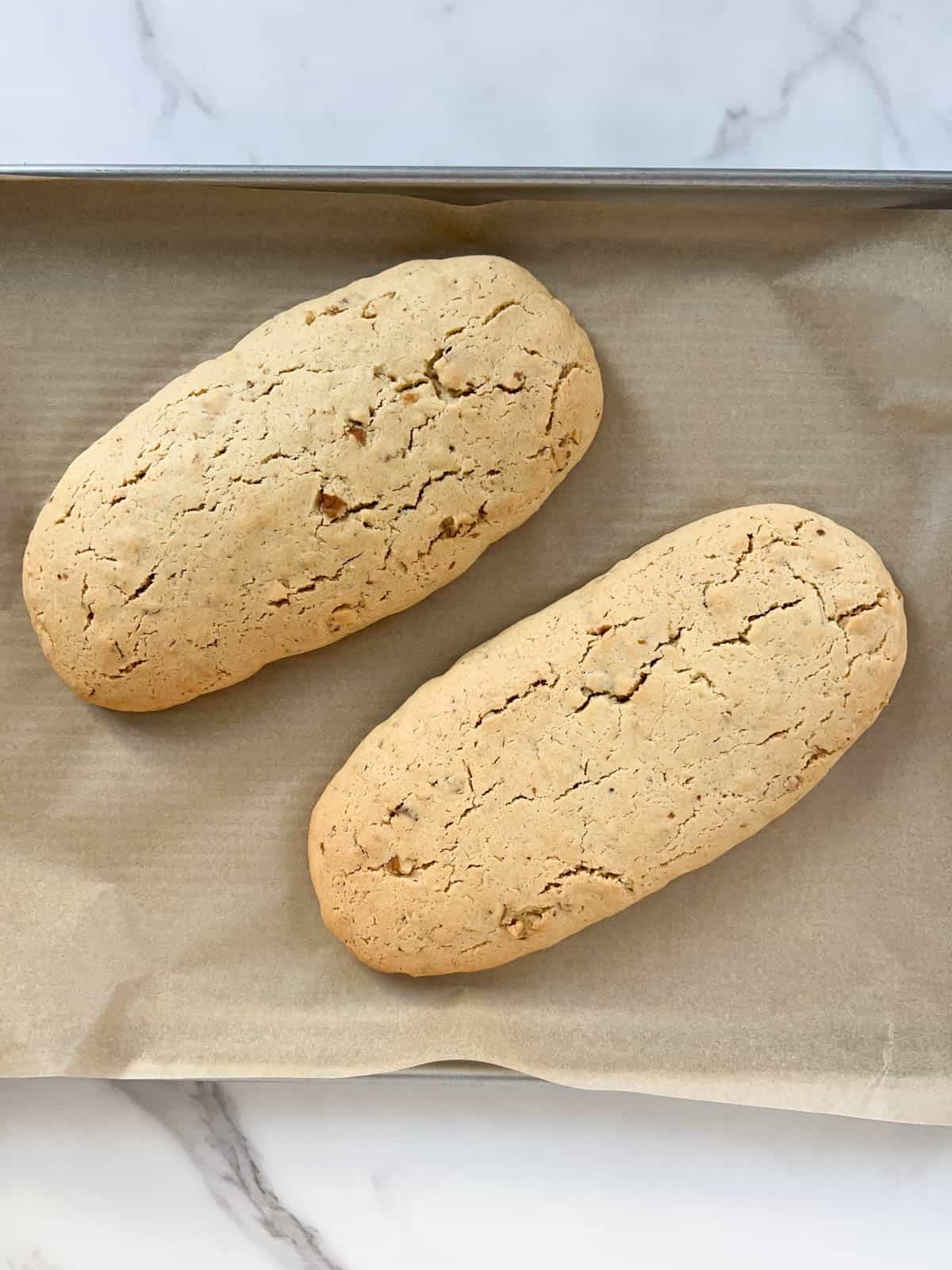 Two baked loaves of walnut biscotti on a metal baking sheet lined with parchment paper.