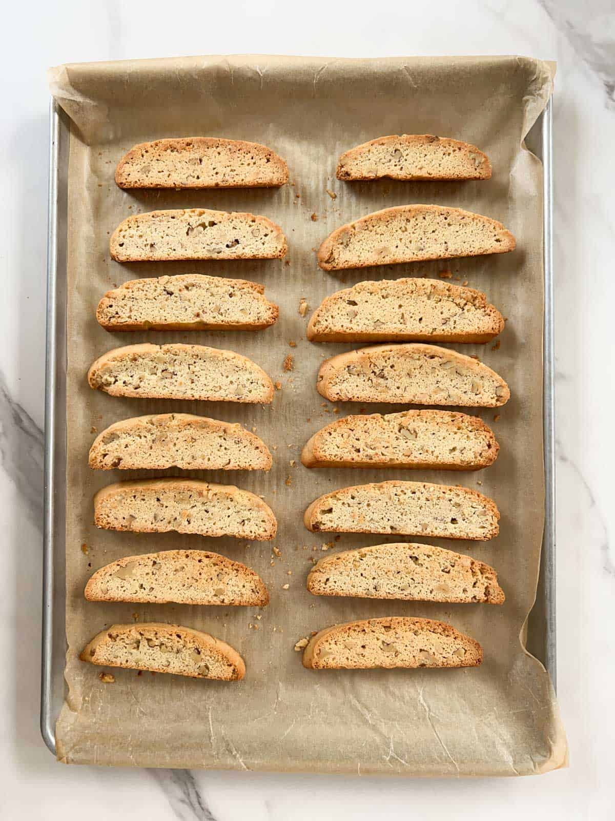 Sixteen slices of baked biscotti on a baking sheet lined with parchment paper.