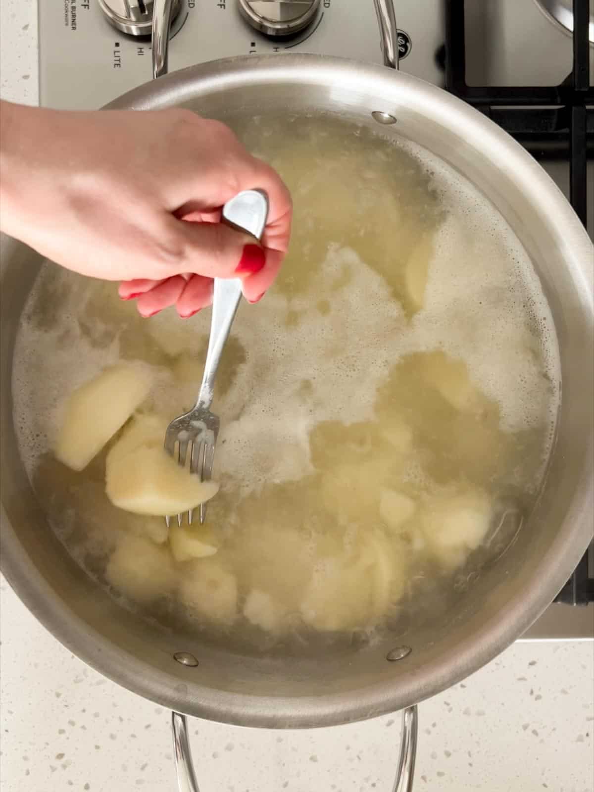 Potatoes boiling in a pot with a fork piercing one of the potatoes.