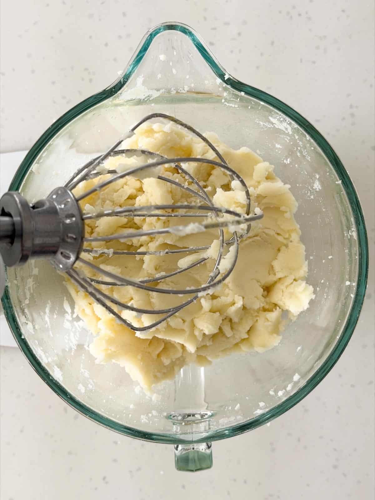 Mashed potatoes in a standing mixer with a whisk attachment.