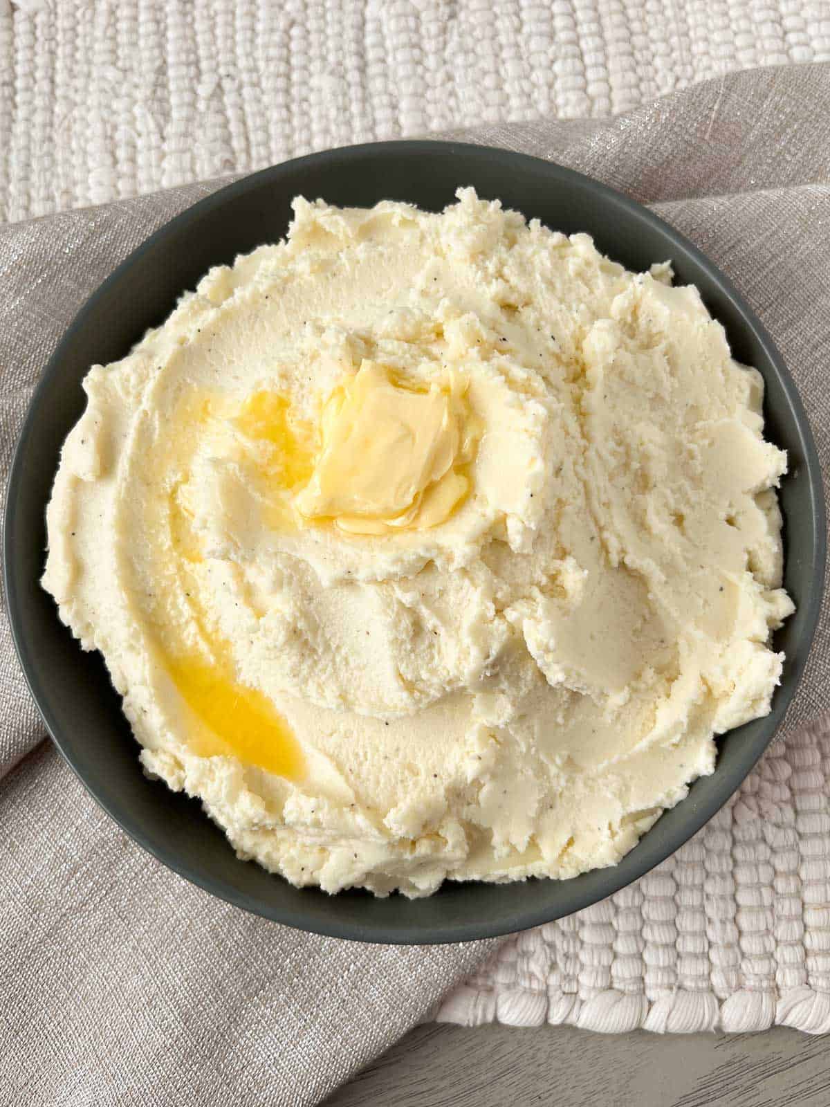 Mashed potatoes topped with melted butter in a serving bowl.