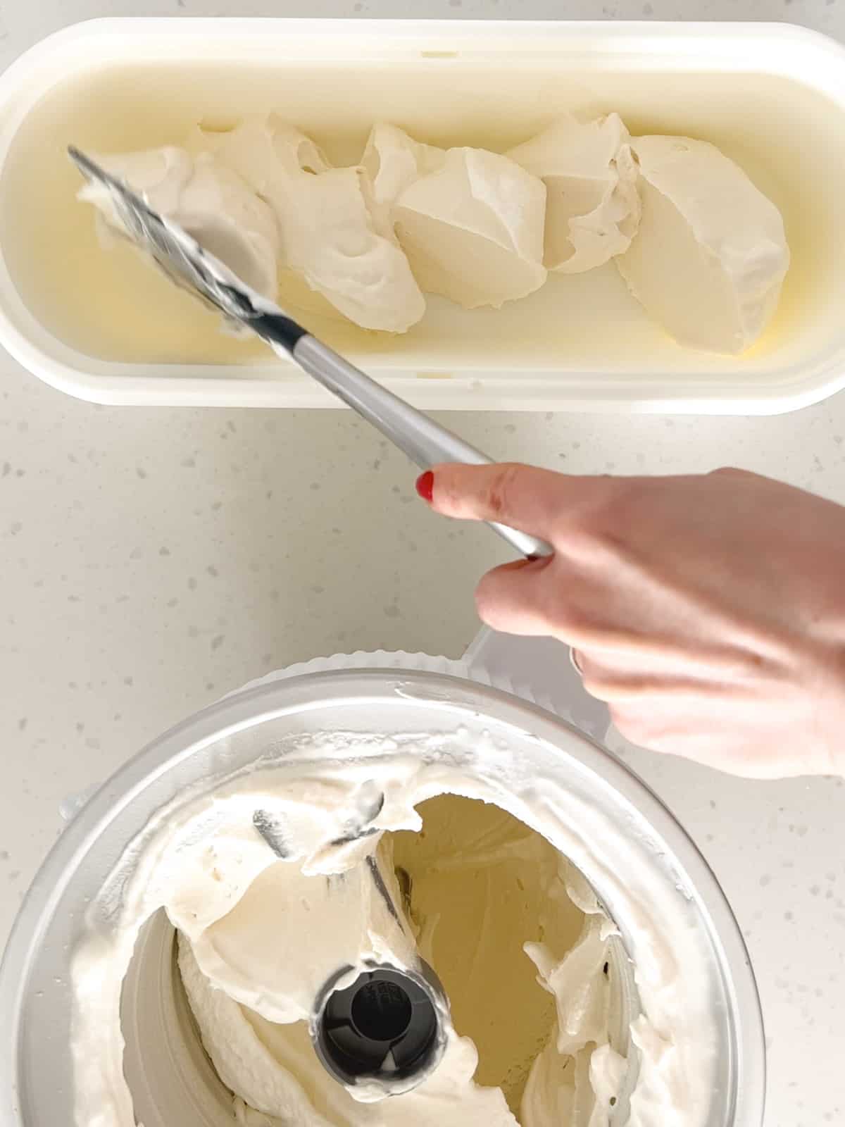 A spatula scoops vanilla ice cream from the ice cream machine into a freezer safe container.