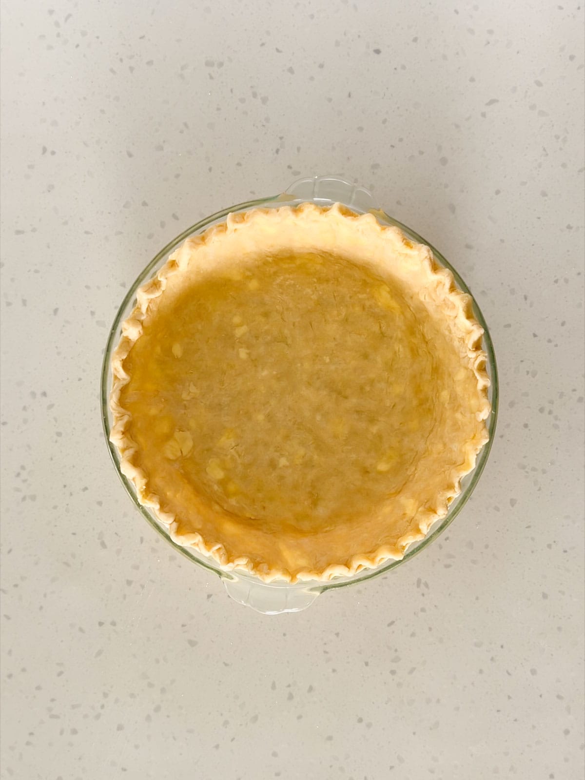 Pie dough with fluted edges in a pie dish.