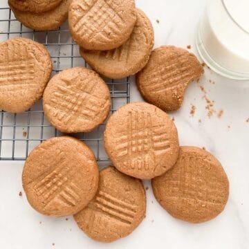 Peanut butter cookies on a metal cooling rack with a glass of milk to the side.