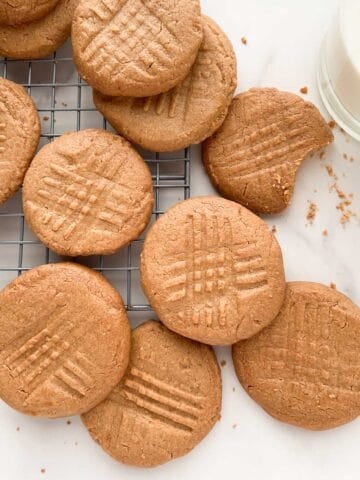 Peanut butter cookies on a metal cooling rack with a glass of milk to the side.