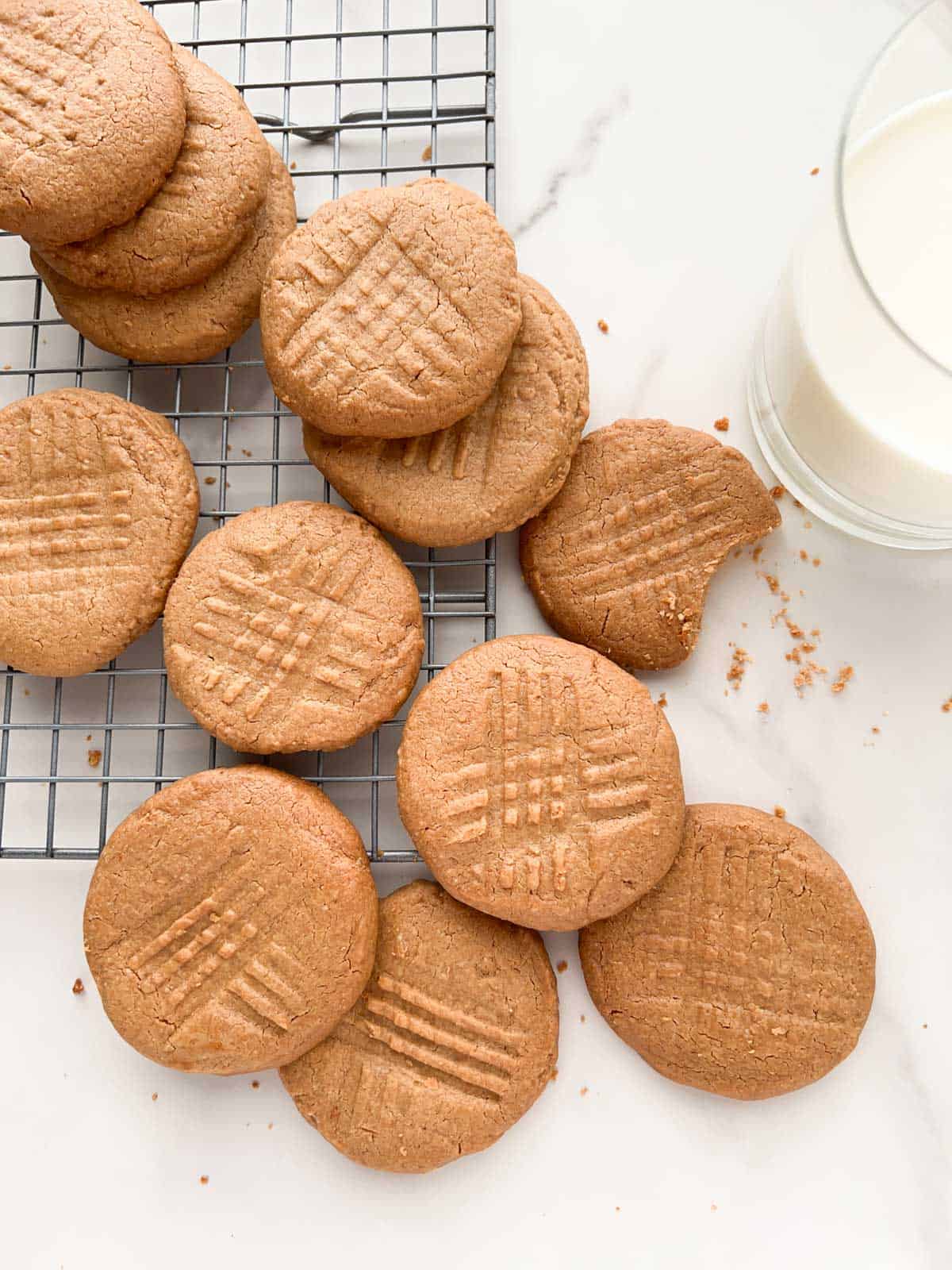 Peanut butter cookies on a cooling rack with a glass of milk to the side.