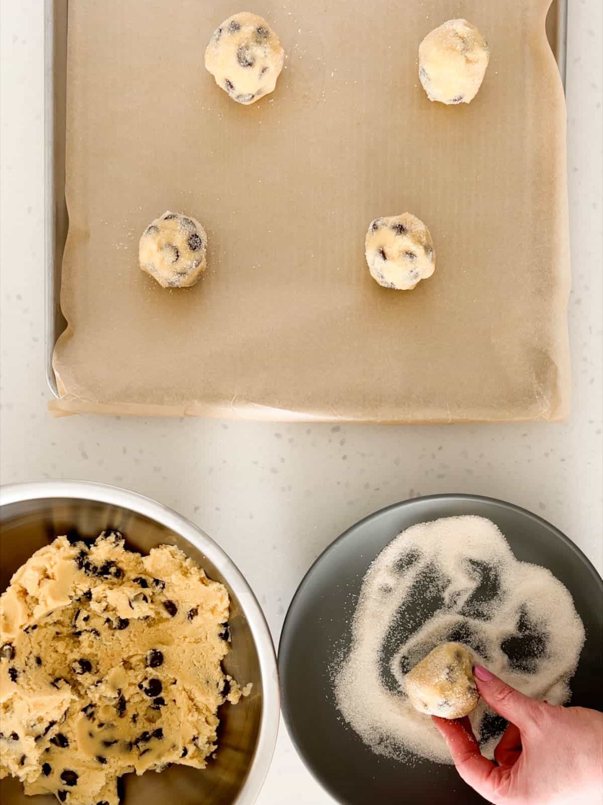 Balls of cookie dough are rolled in sugar and placed on a baking sheet.