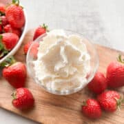 A bowl of whipped cream surrounded by strawberries.
