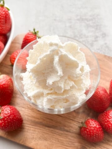 A bowl of whipped cream surrounded by strawberries.
