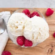 Two scoops of vanilla ice cream garnished with raspberries.