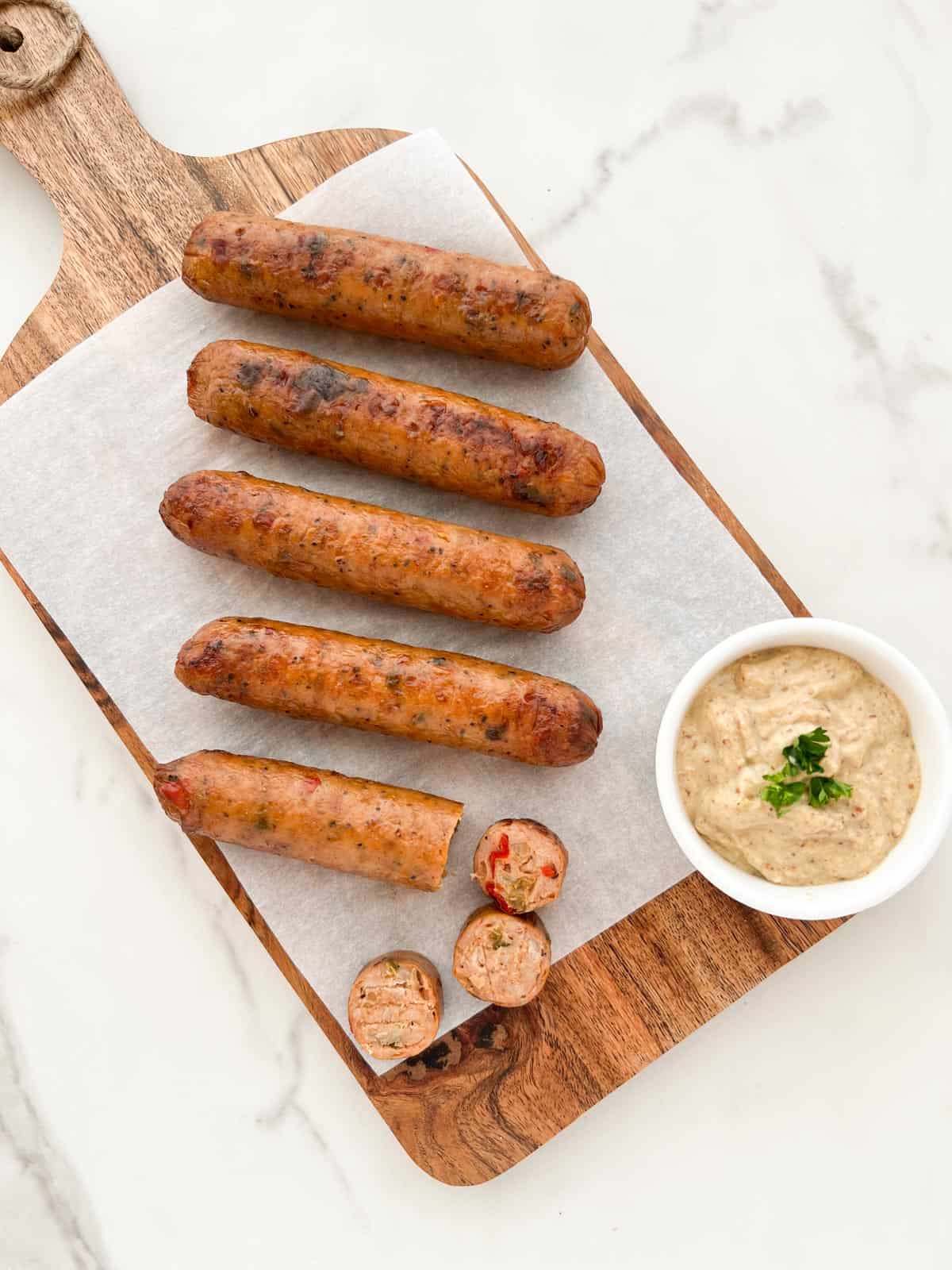 Chicken sausages served on a wood tray with mustard dip.
