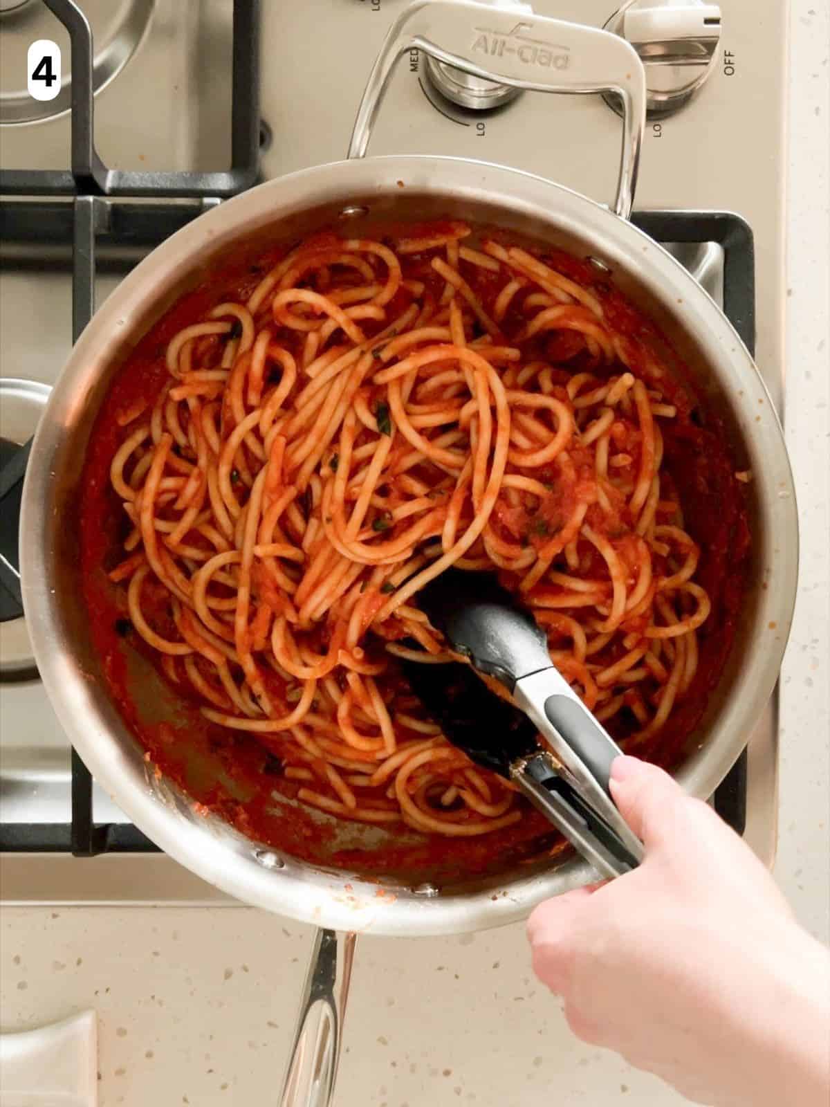 Bucatini and pomodoro sauce are mixed together in a pan.