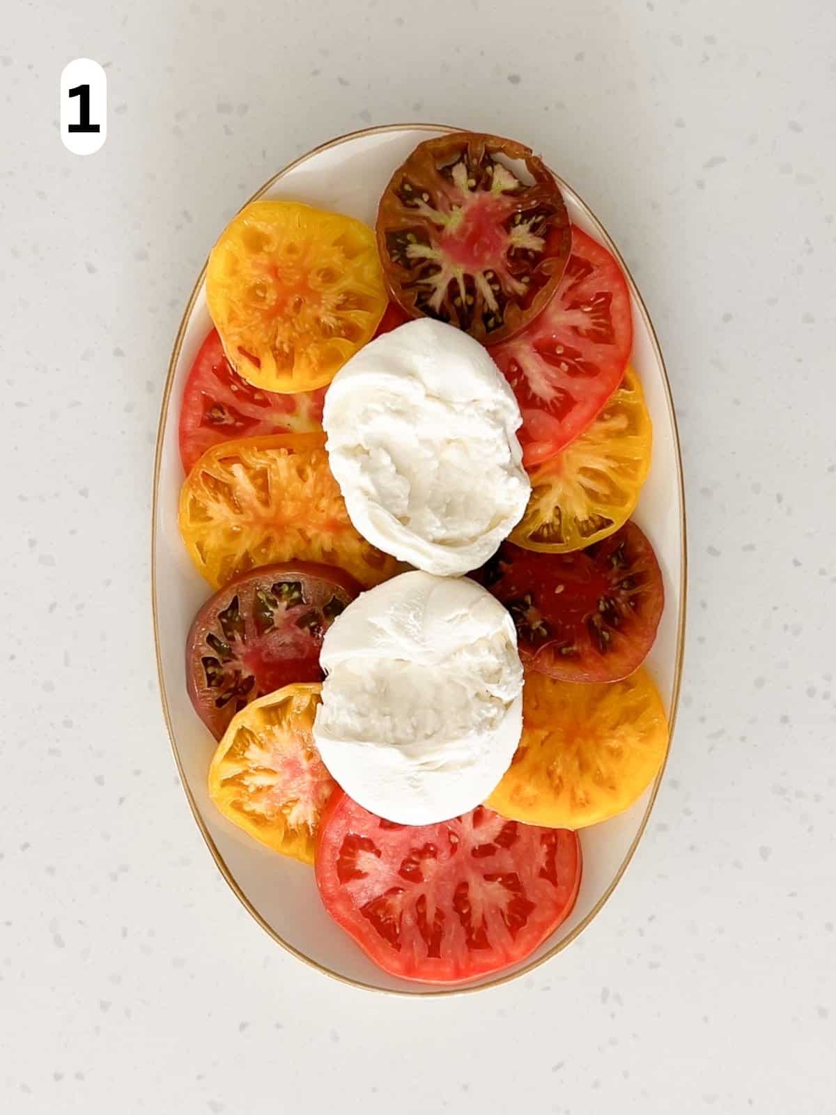 The tomato slices are arranged on a platter with two balls of burrata in the center.