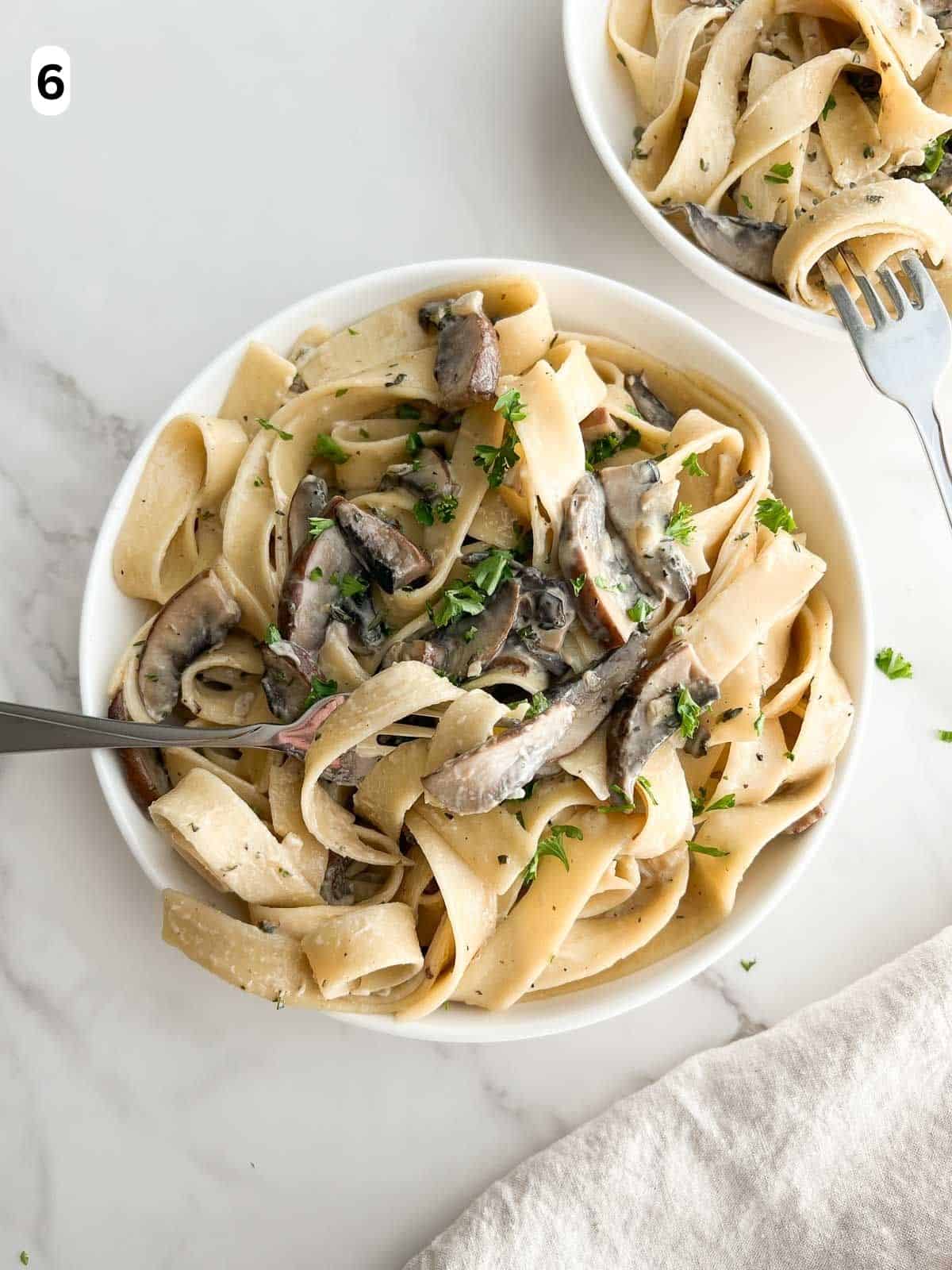 Two bowls of mushroom pappardelle are garnished with parsley and Parmigiano-Reggiano.