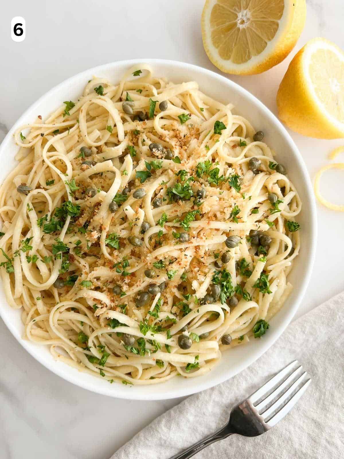 A bowl of lemon caper pasta garnished with Italian breadcrumbs and parsley.