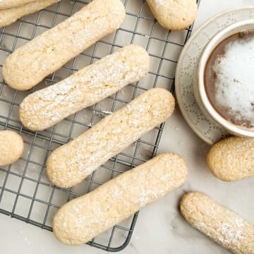 Savoiardi (Italian ladyfingers) on a cooling rack with a latte to the side.