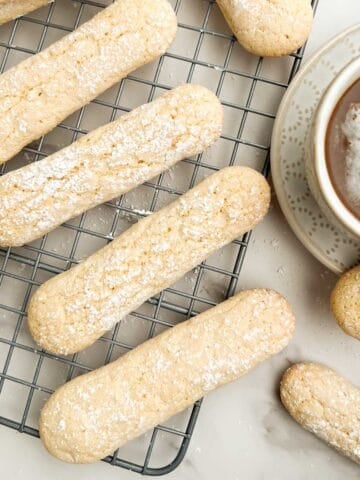 Savoiardi (Italian ladyfingers) on a cooling rack with a latte to the side.