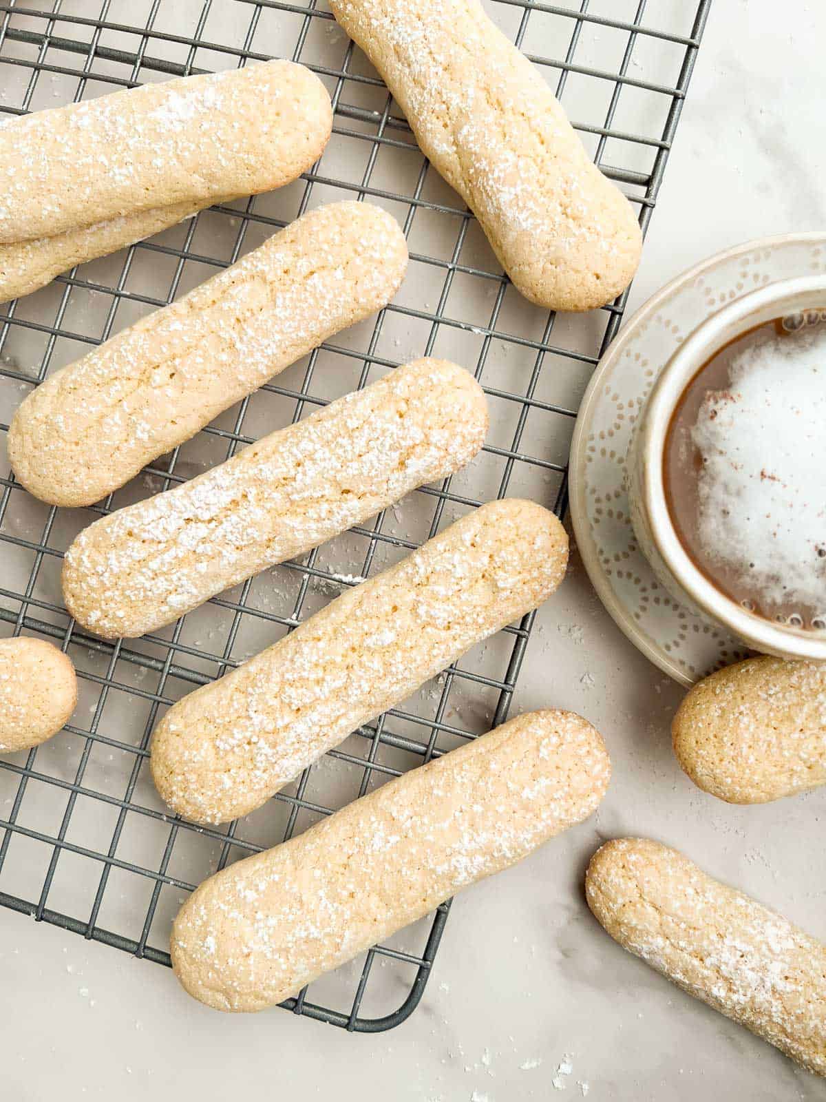 Savoiardi (Italian ladyfingers) on a cooling rack with a latte to the side.