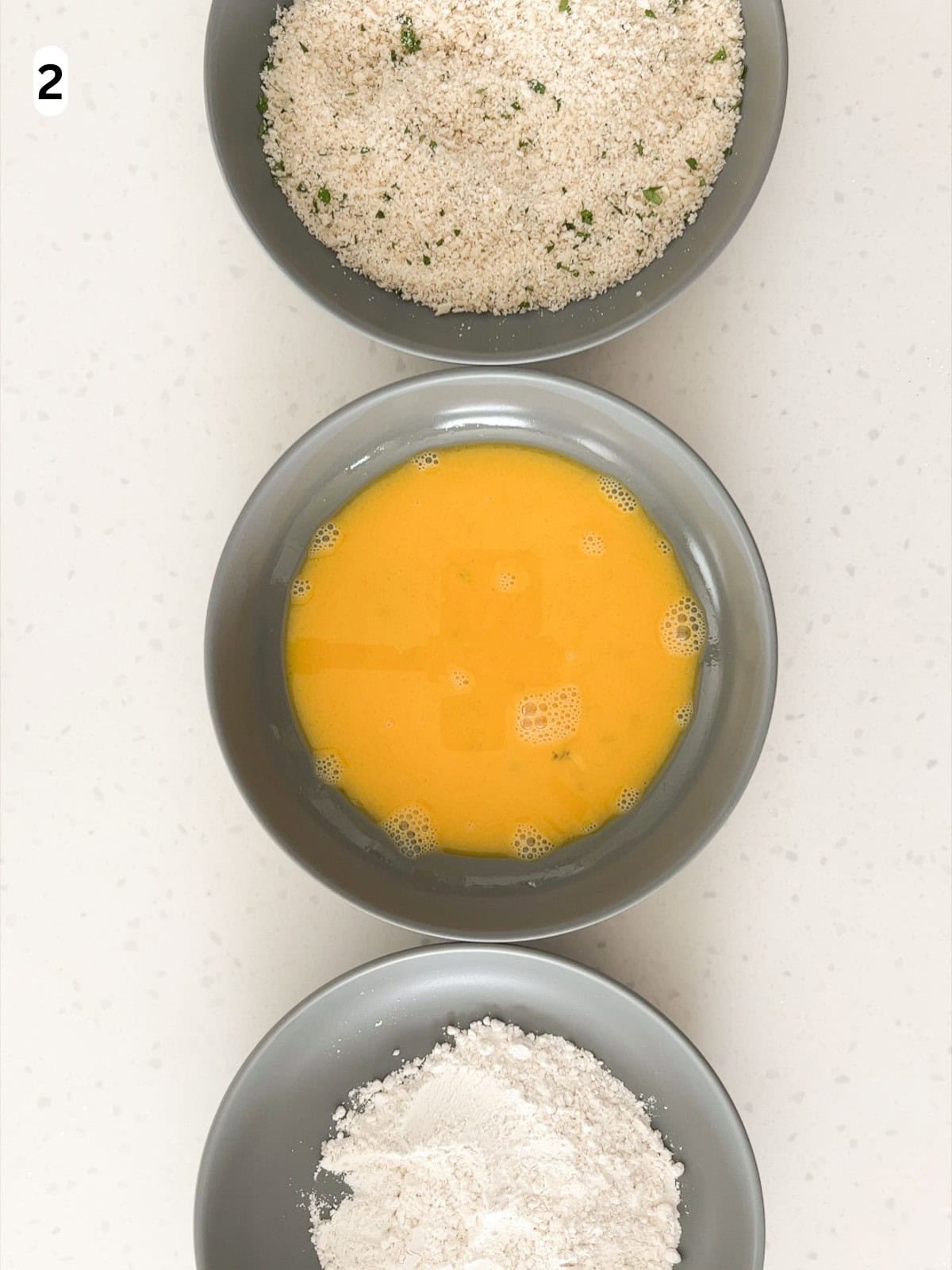 Three breading stations are arranged with the flour first, the egg mixture second, and breadcrumbs third.