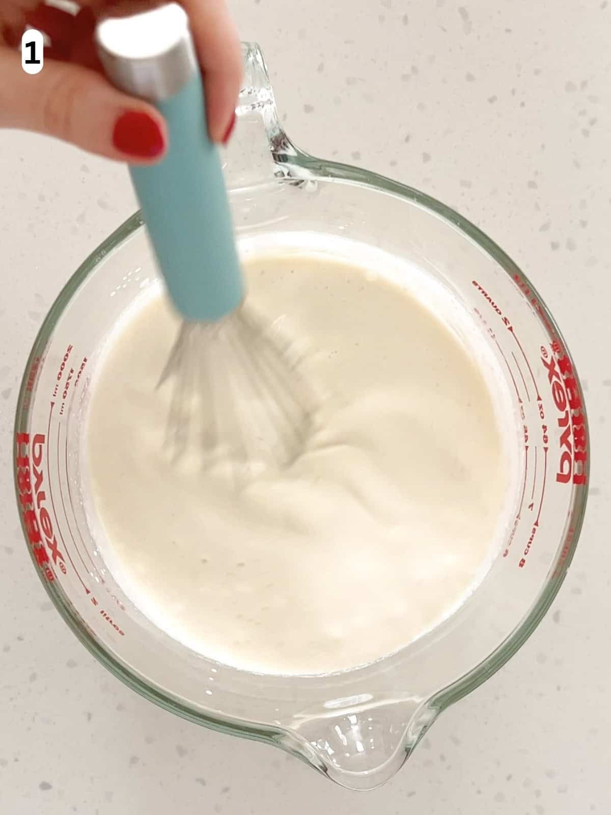 The ingredients for no egg vanilla ice cream are whisked together in a measuring cup.